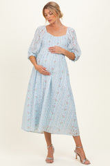 woman wearing a light blue floral maternity dress with a square neckline and puff sleeves, cradling her baby bump