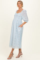 woman wearing a light blue floral maternity dress with puff sleeves and pockets, featuring a fitted bodice and flowing skirt