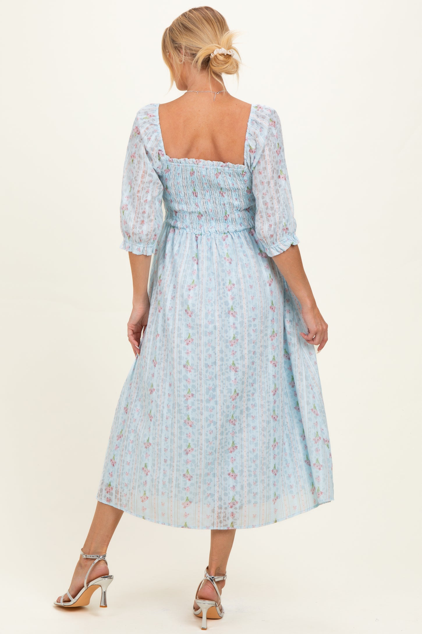 woman wearing a light blue floral maternity dress with short puffed sleeves and a smocked bodice, shown from the back