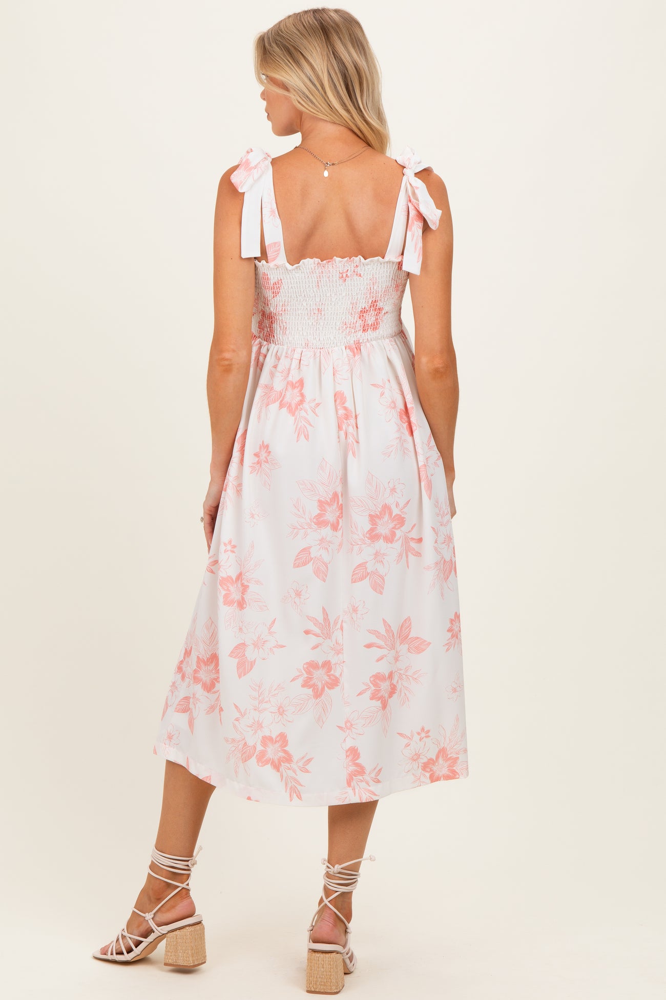 woman wearing a white floral maternity dress with a smocked bodice and tied straps, showing her back