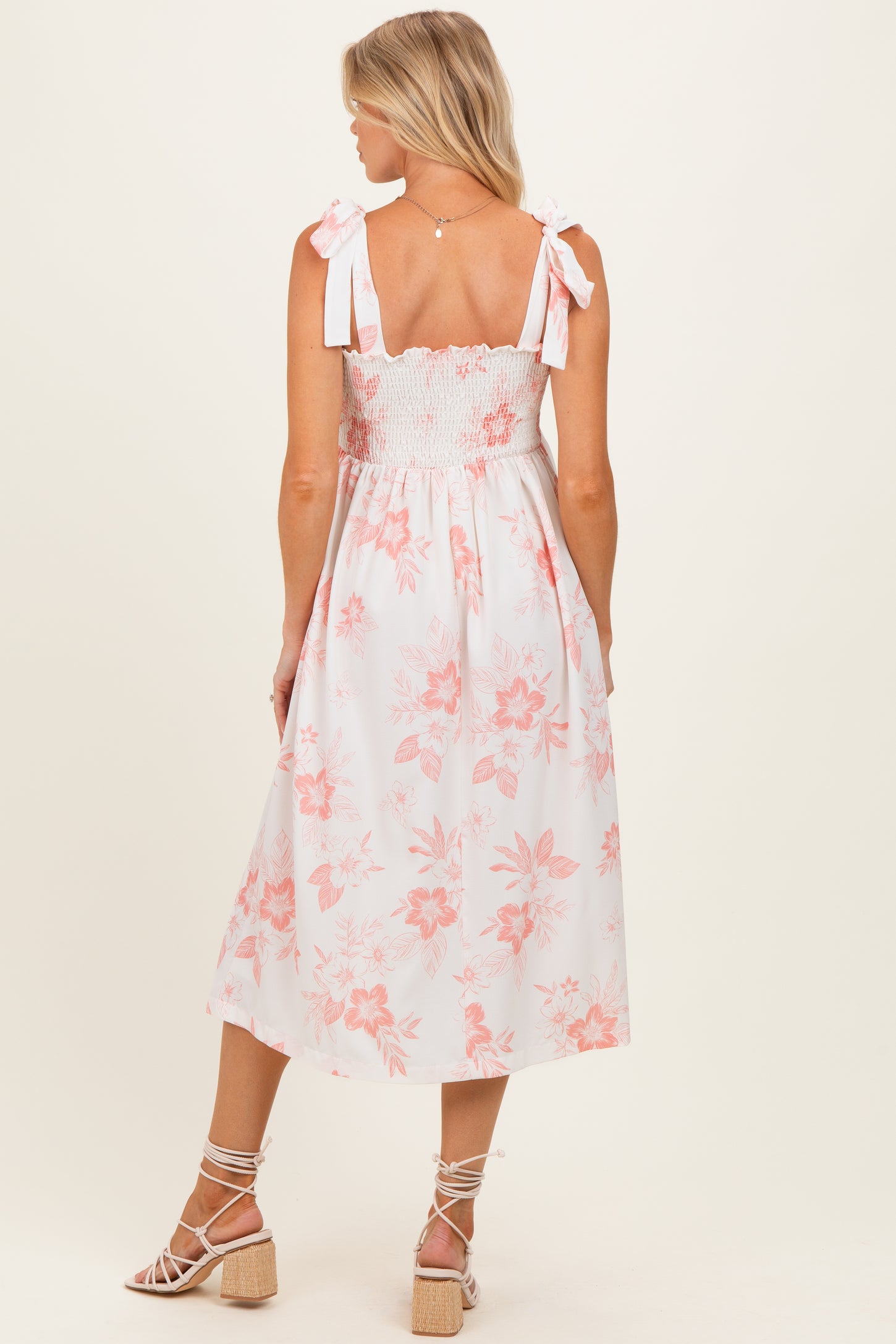 woman wearing a white floral maternity dress with a smocked bodice and tied straps, showing her back