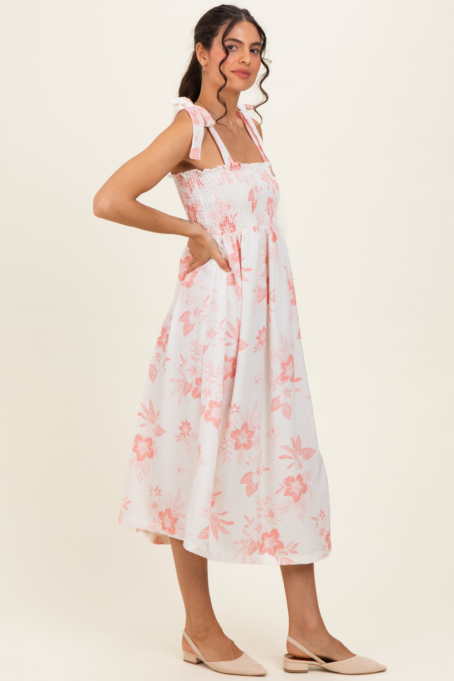 woman wearing a pink floral smocked midi dress with tie straps and pockets