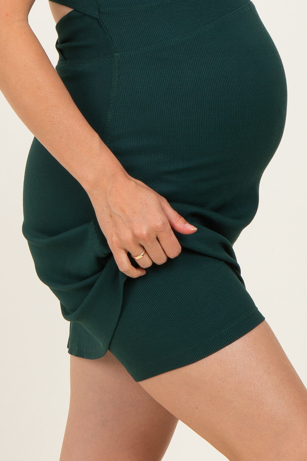 woman wearing a dark green ribbed maternity dress showing her baby bump and holding the fabric gently