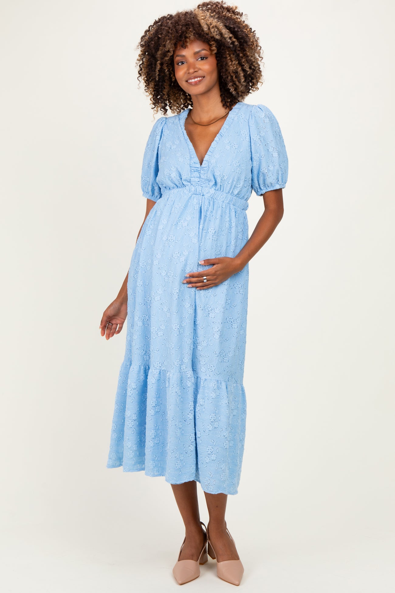woman wearing a light blue maternity dress with puff sleeves and a tiered skirt, cradling her baby bump