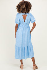 woman wearing a sky blue maternity dress with puffed sleeves and a tiered skirt, showing the back view