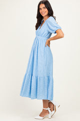 woman wearing a light blue midi dress with puff sleeves and a tiered hem, standing in a profile pose