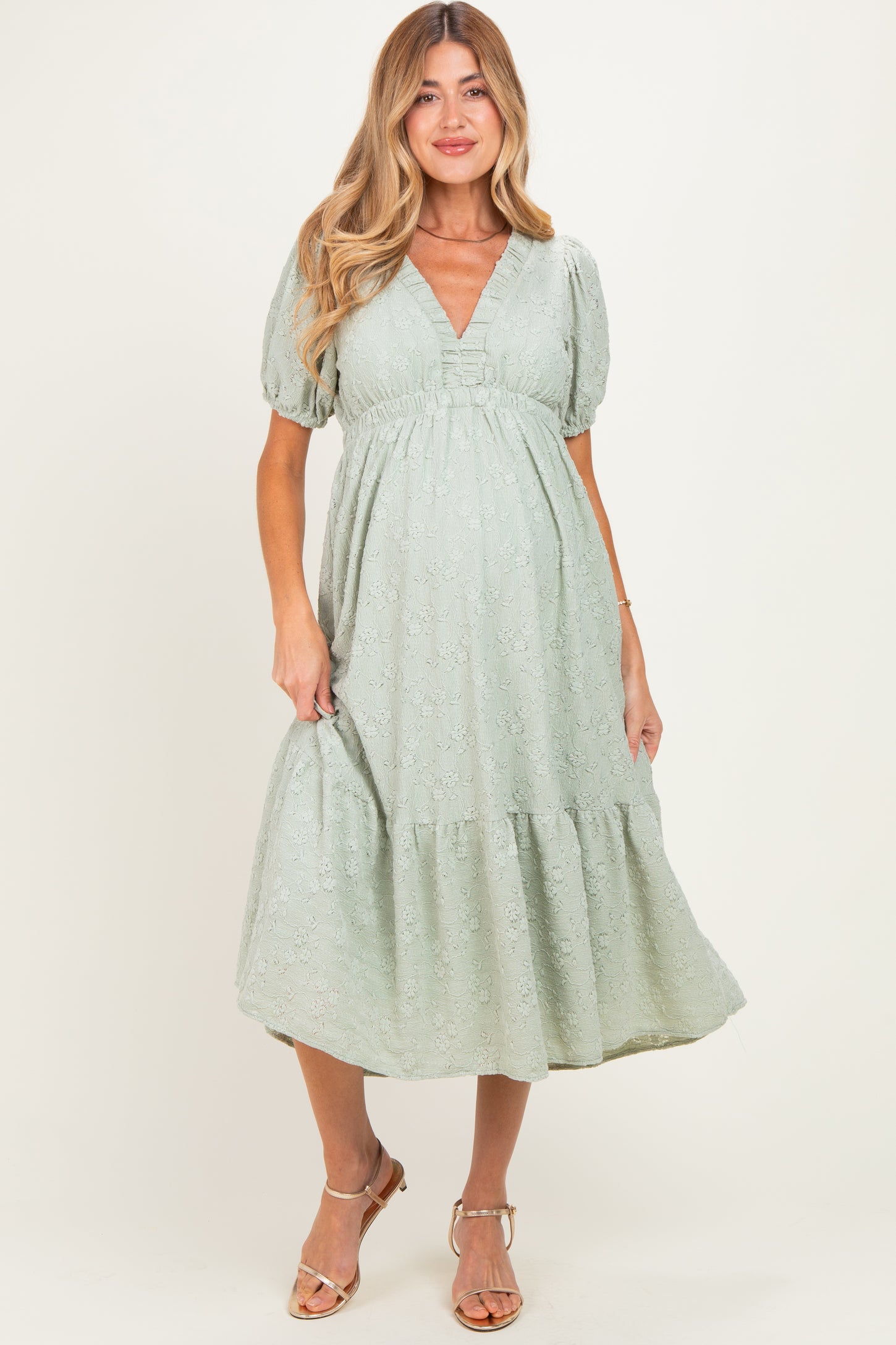 woman wearing a light green short sleeve maternity dress with a v-neck and tiered skirt, showcasing her baby bump