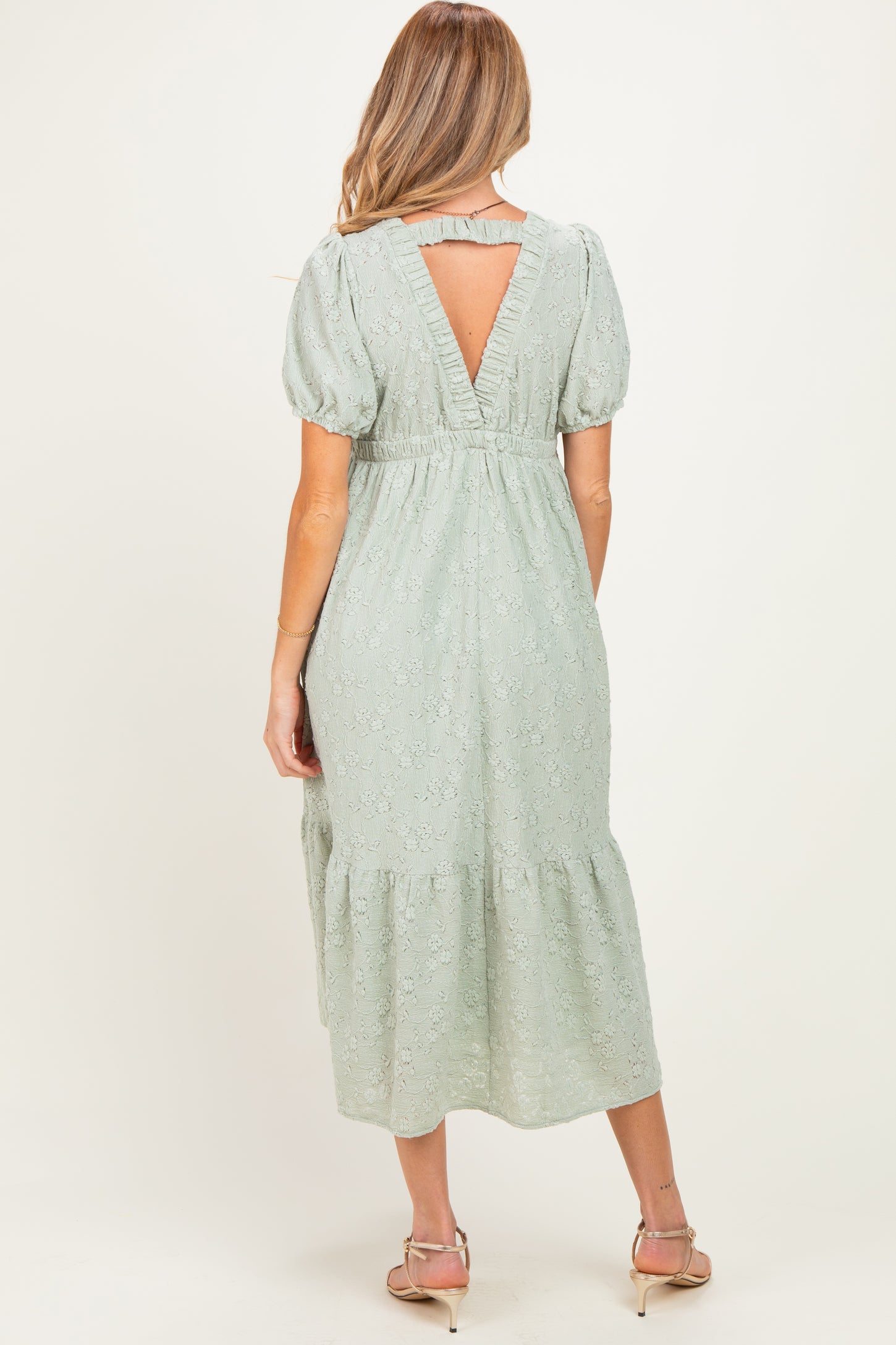 woman wearing a light green maternity midi dress with puff sleeves and a back cutout detail