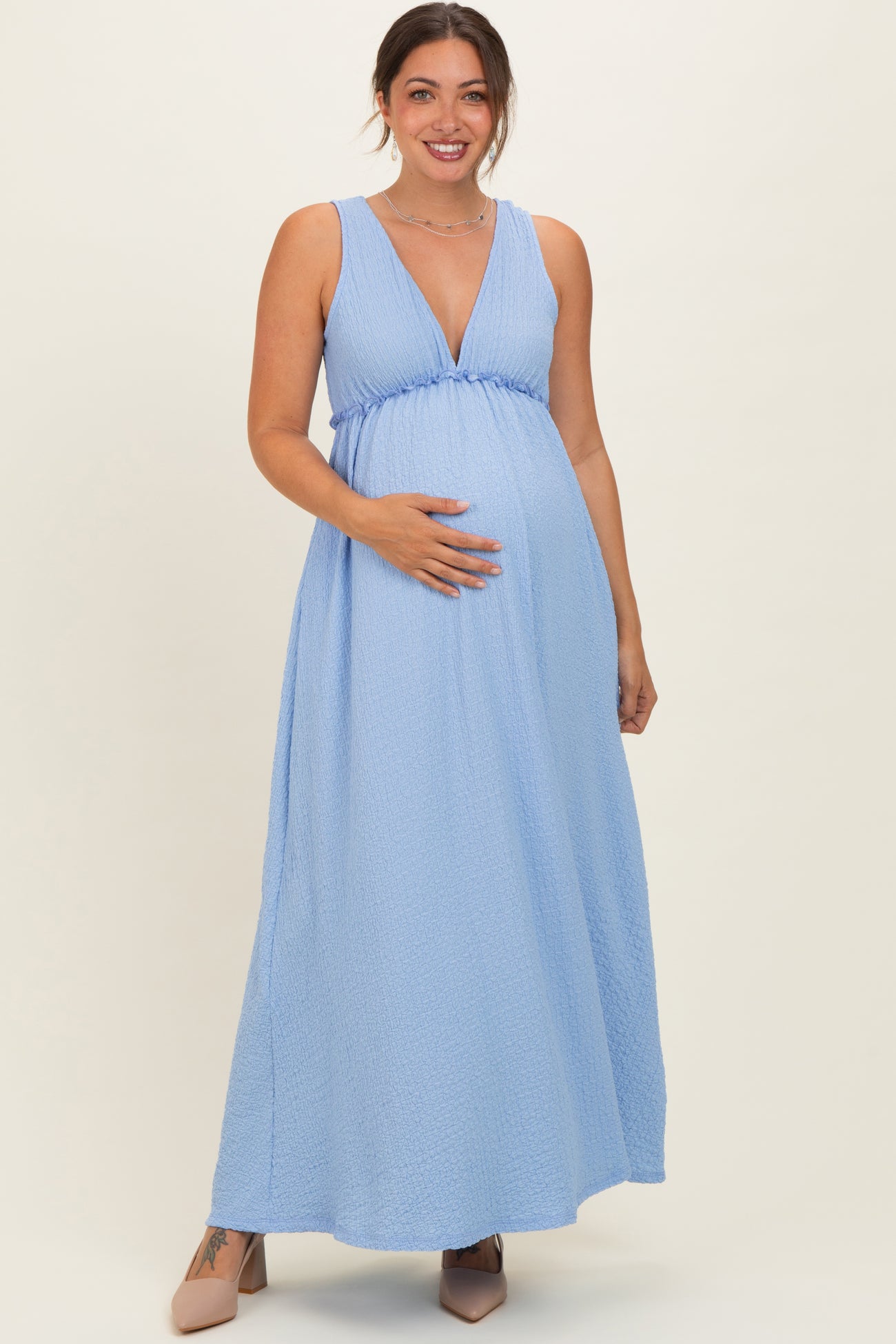 woman wearing a light blue sleeveless maxi maternity dress with a plunging neckline and holding her baby bump