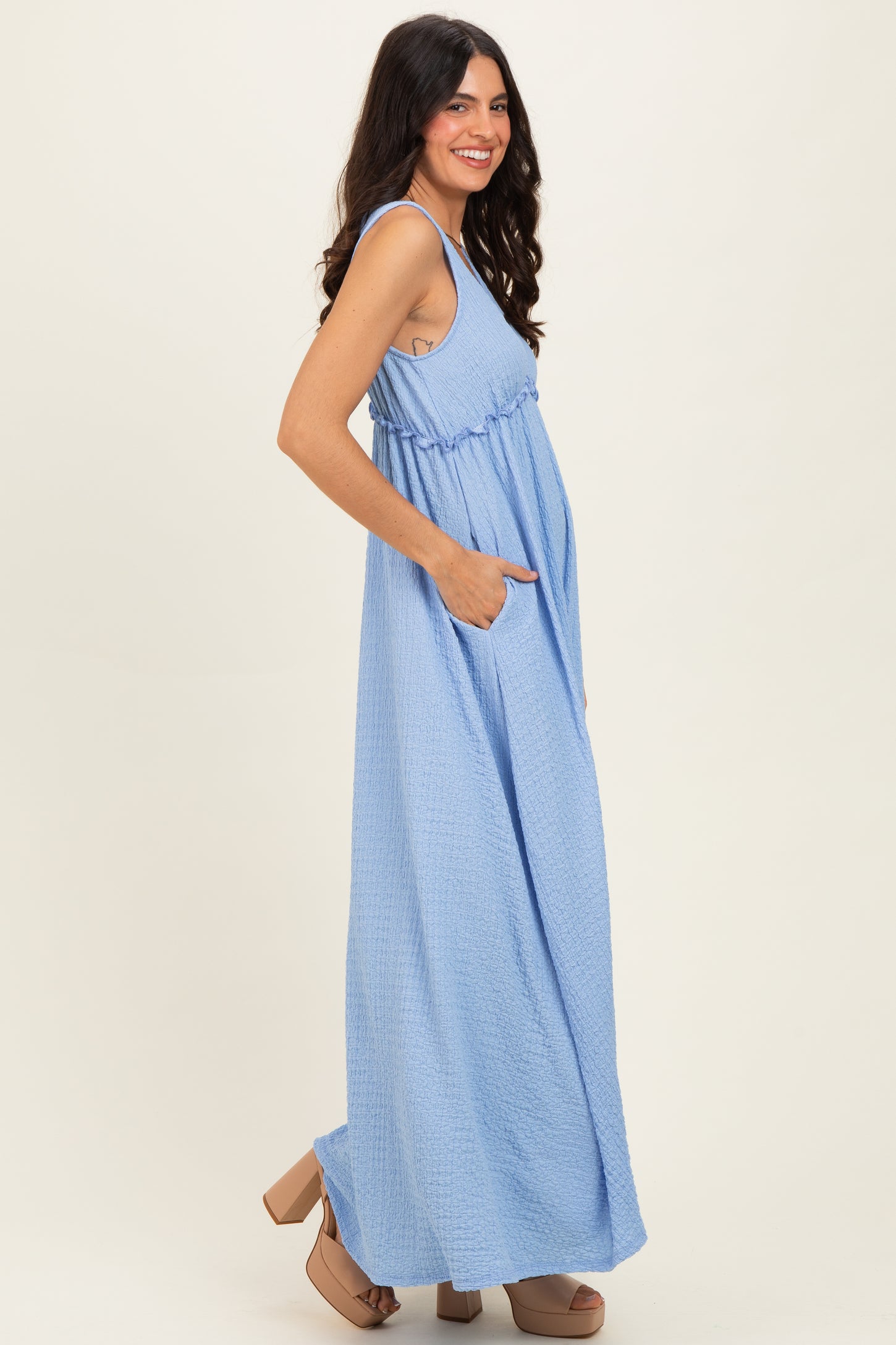 woman wearing a light blue maxi dress with pockets and a gathered waist, standing in profile