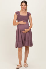 woman wearing a mauve maternity dress with ruffled sleeves and a smocked bodice, gently holding her baby bump