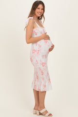 woman wearing a light pink floral maternity dress with a fitted bodice and ruffled hem, holding her baby bump