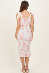 woman wearing a white and pink floral shirred maternity dress with tie straps and a ruffled hem, showing a baby bump