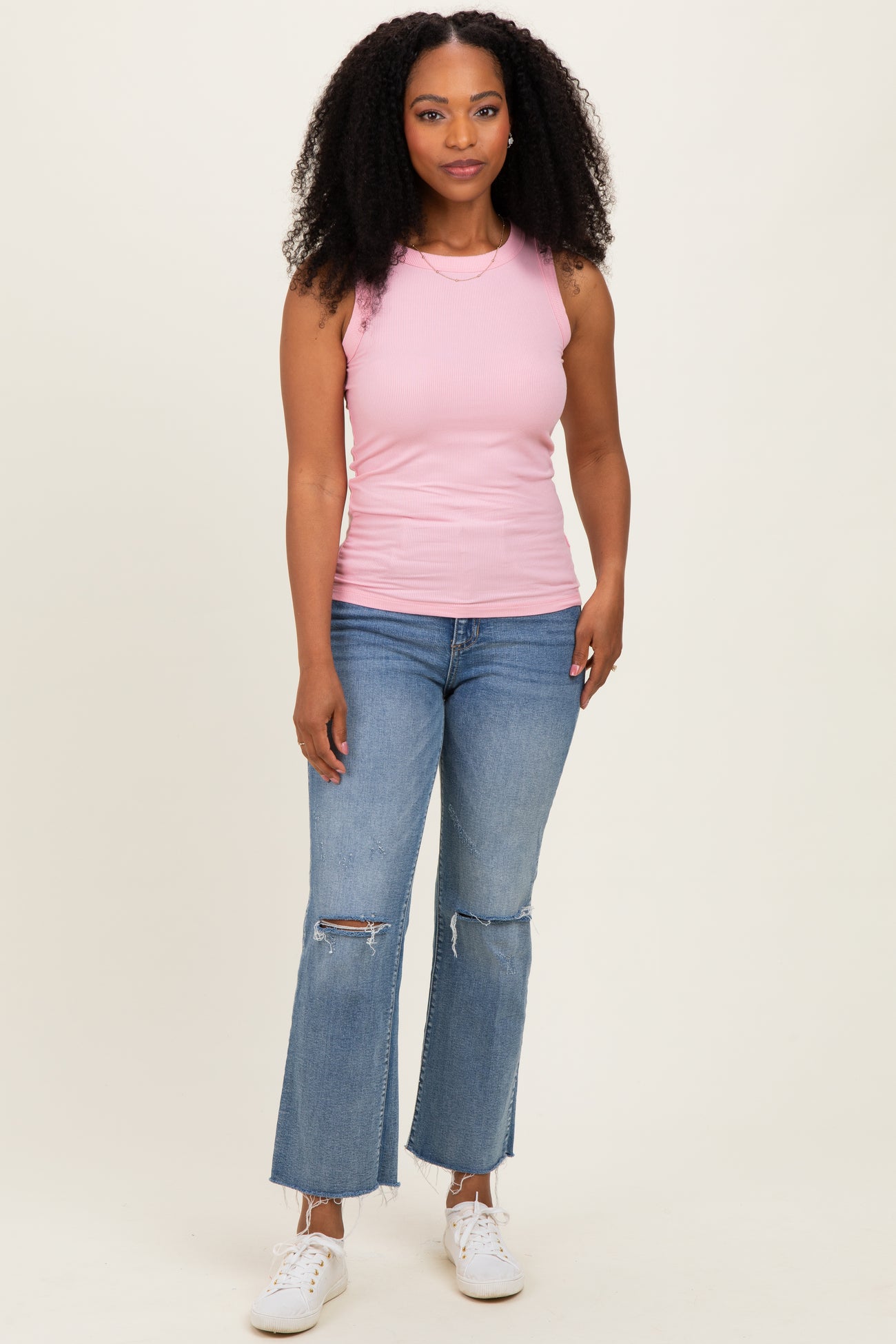 woman wearing a light pink ribbed tank top and distressed flared jeans with white sneakers