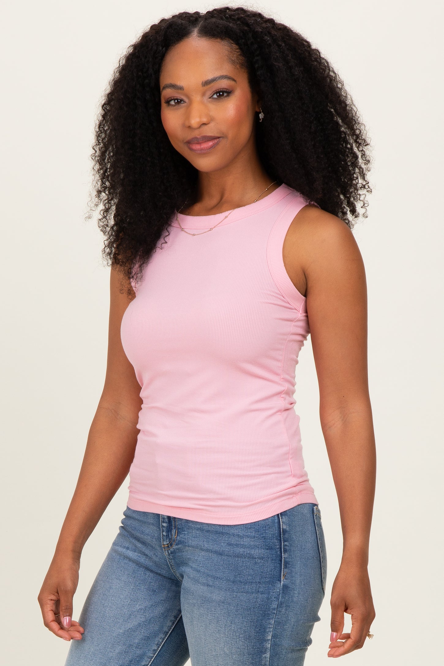 woman wearing a light pink sleeveless ribbed top and blue jeans