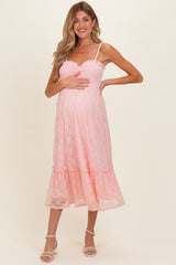 woman wearing a pink lace maternity dress with a fitted bodice and tiered skirt, holding her baby bump