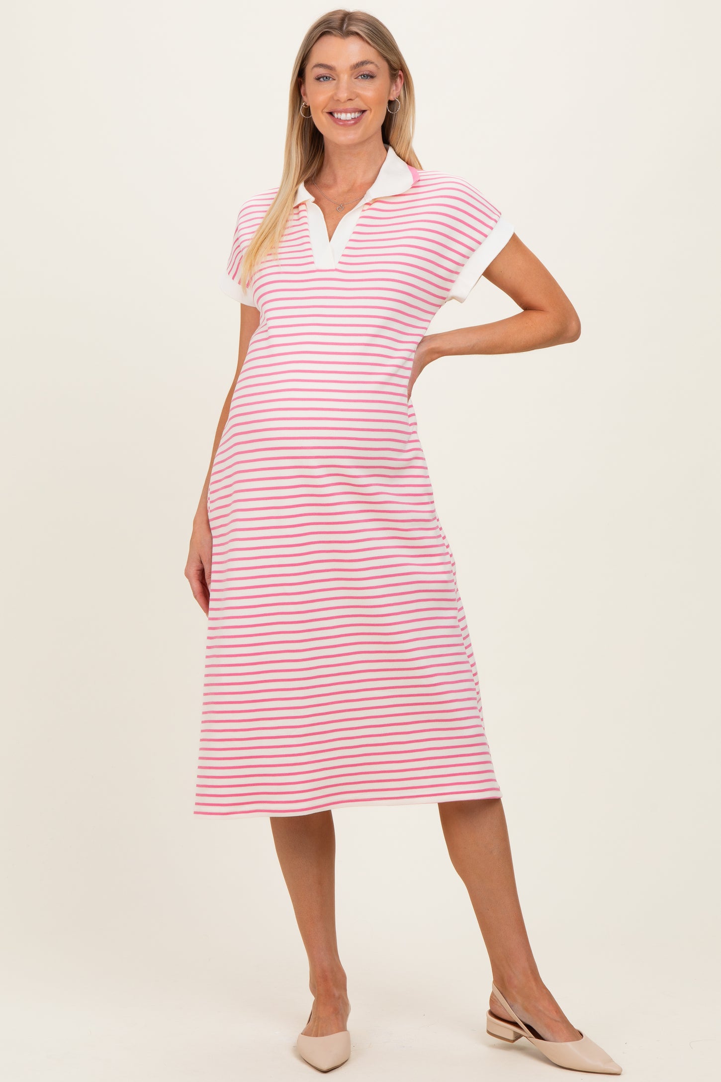 woman wearing a pink and white striped maternity polo dress with a collar and short sleeves, showcasing her baby bump