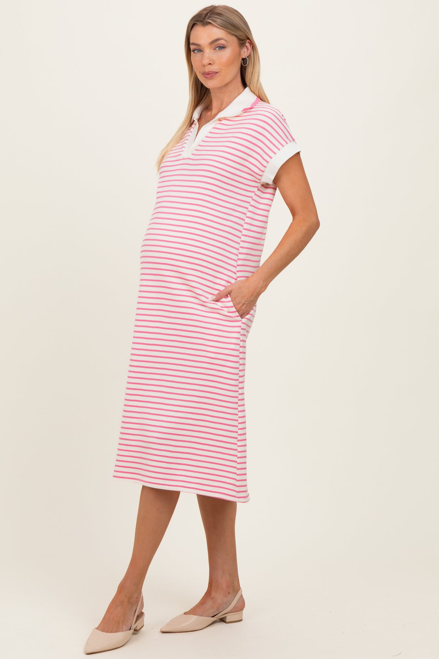 woman wearing a pink and white striped maternity dress with short sleeves and pockets, showcasing her baby bump