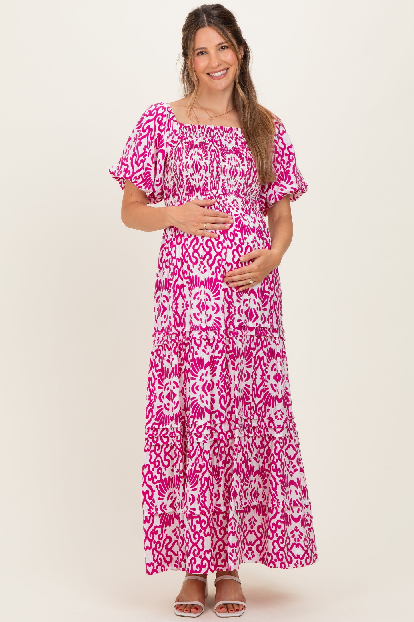 woman wearing a pink and white patterned maternity maxi dress and holding her baby bump