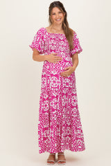woman wearing a pink and white patterned maternity maxi dress and holding her baby bump