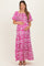 woman wearing a pink and white patterned maternity maxi dress and holding her baby bump