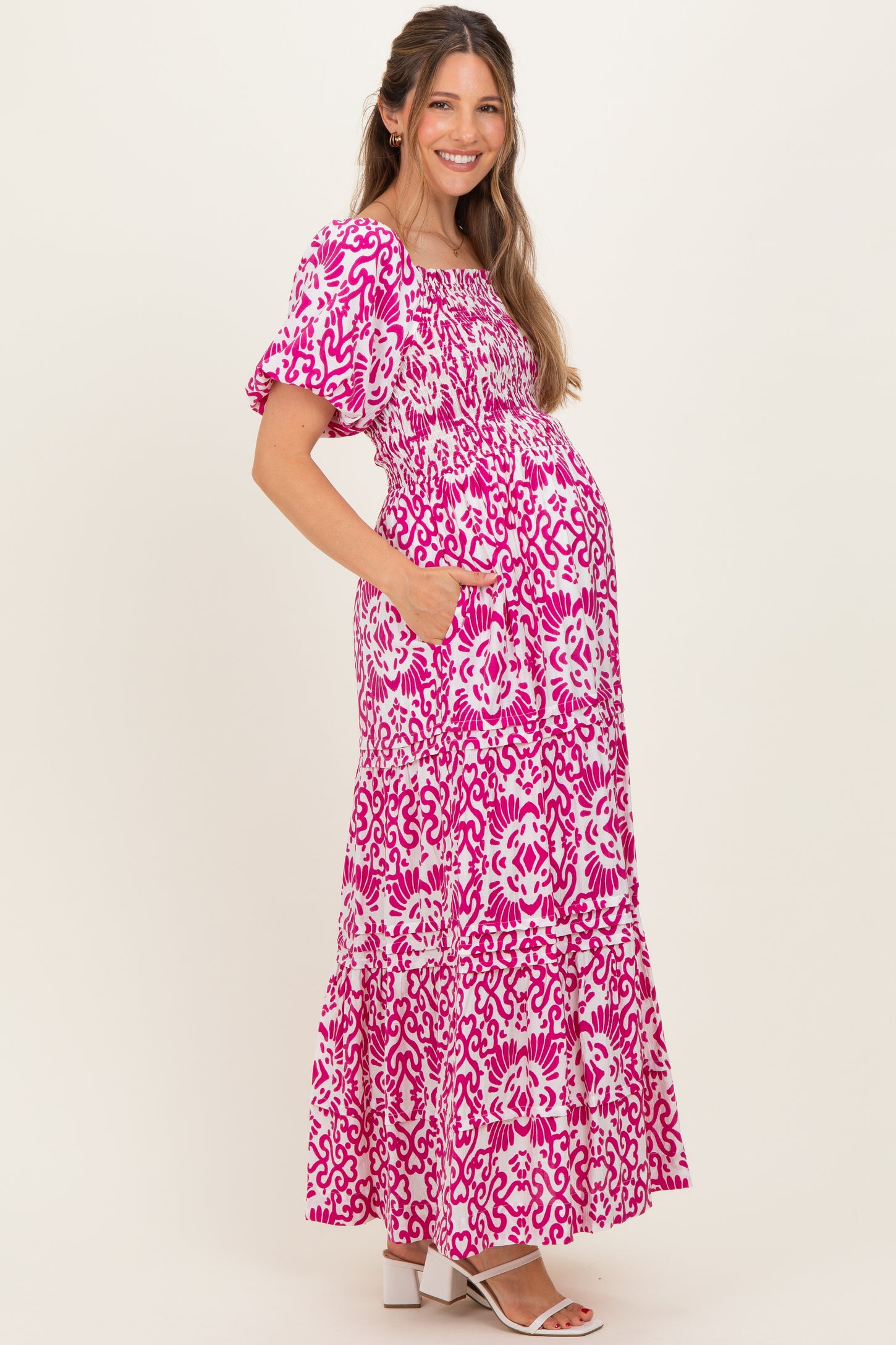 woman wearing a pink and white floral print maternity maxi dress with puff sleeves and pockets, showing her baby bump