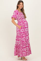 woman wearing a pink and white floral print maternity maxi dress with puff sleeves and pockets, showing her baby bump