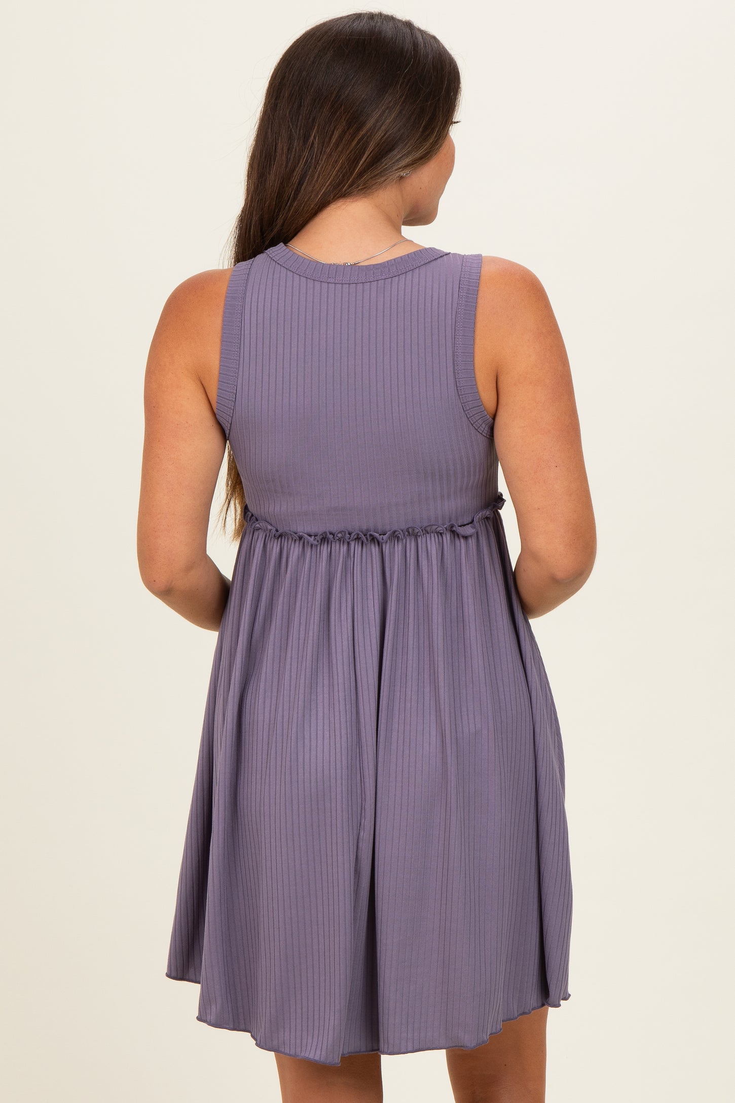 woman wearing a lavender sleeveless maternity dress with a tie waist and a flowy skirt, showing her baby bump from the back