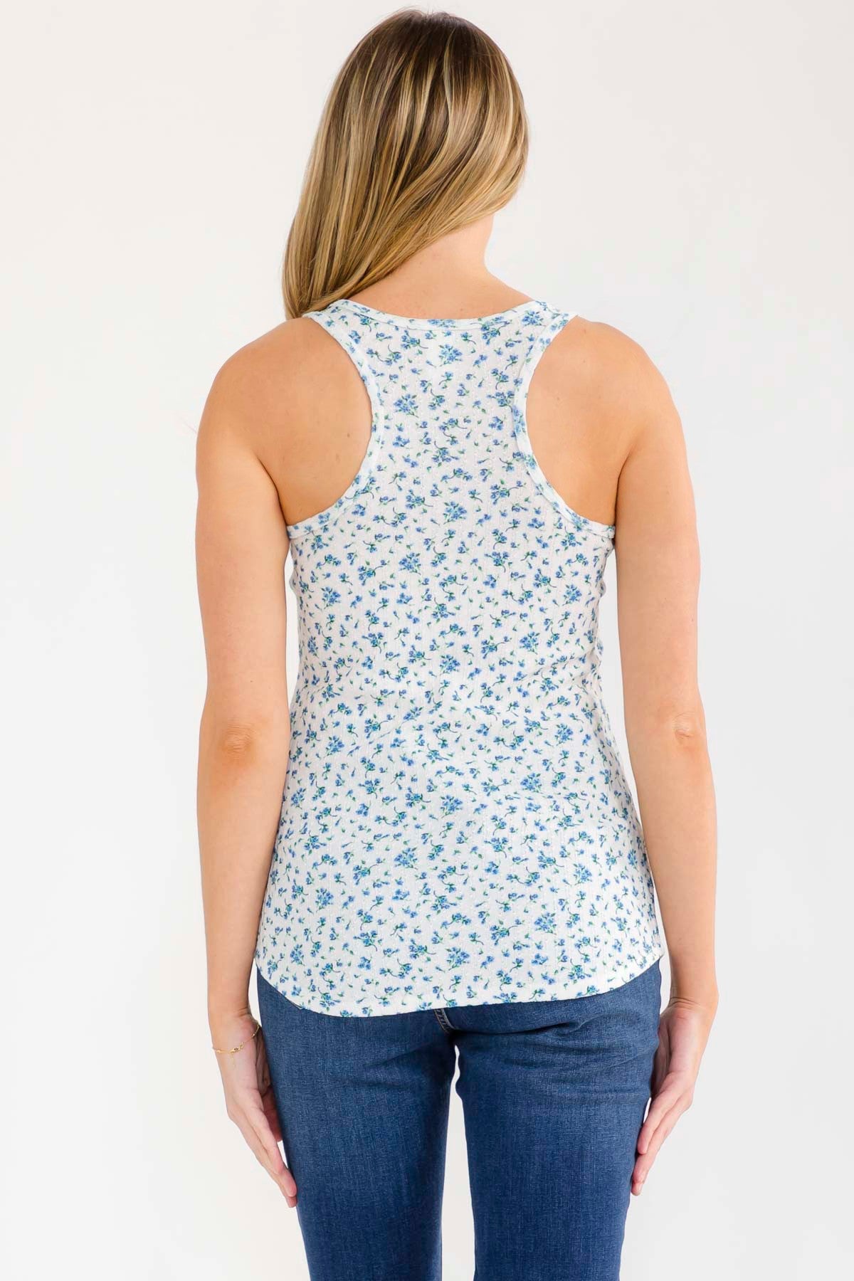 woman wearing a white tank top with small blue floral prints and blue jeans, viewed from the back