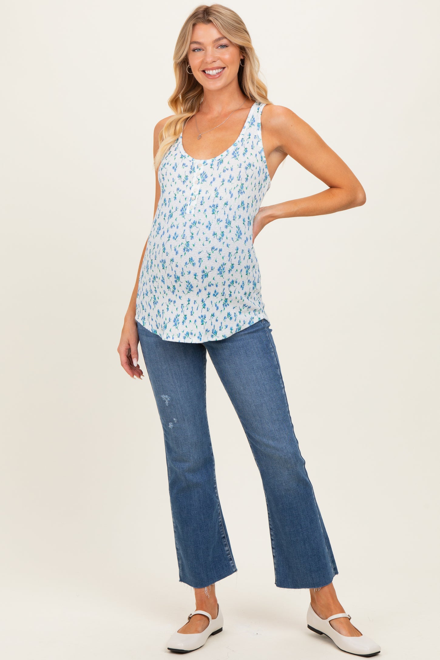 woman wearing a blue floral maternity tank top and flared jeans, showing her baby bump