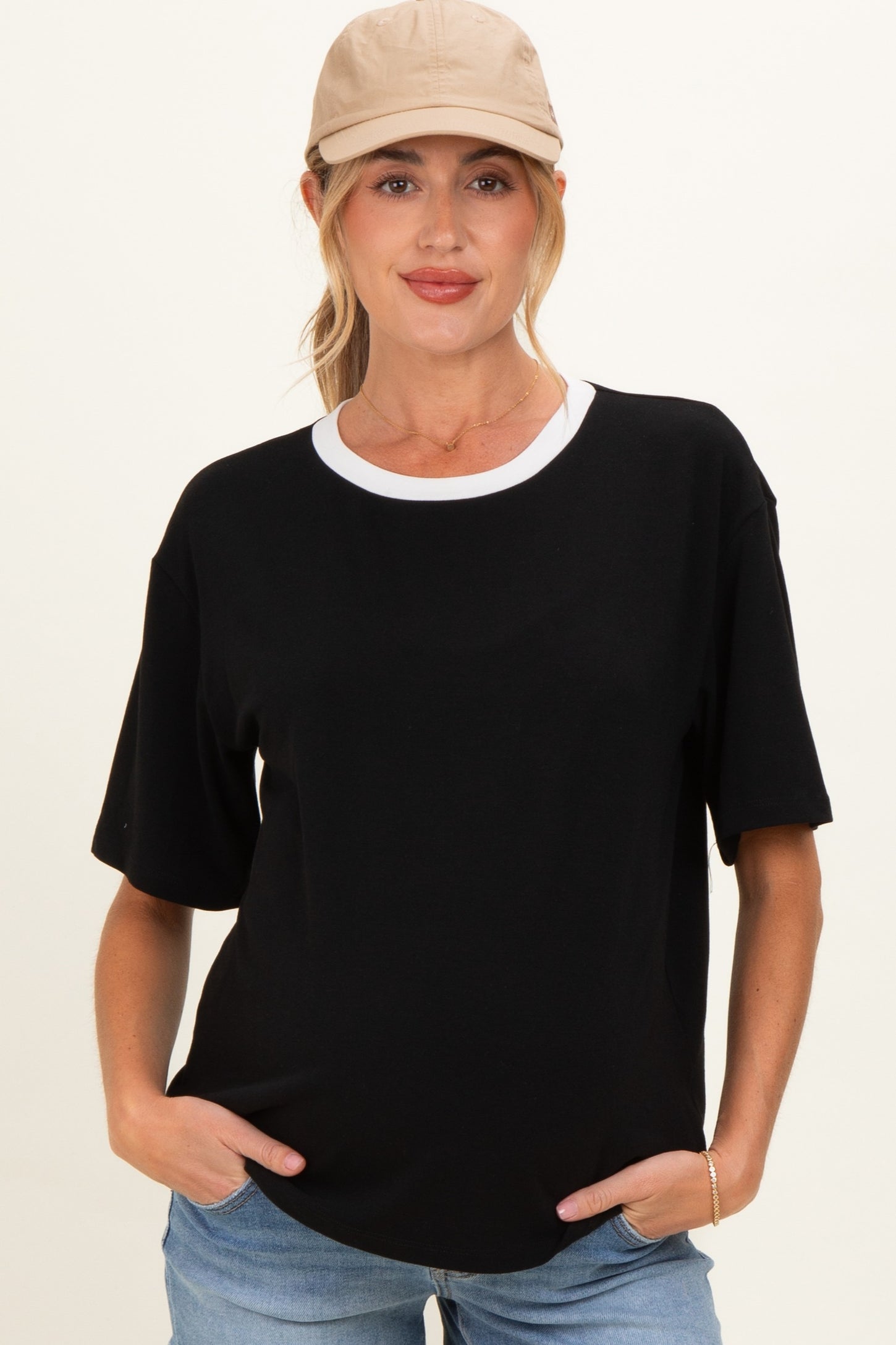 woman wearing a black short sleeve maternity top with a white collar and holding her hands in the pockets of her jeans