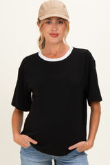 woman wearing a black short sleeve maternity top with a white collar and holding her hands in the pockets of her jeans