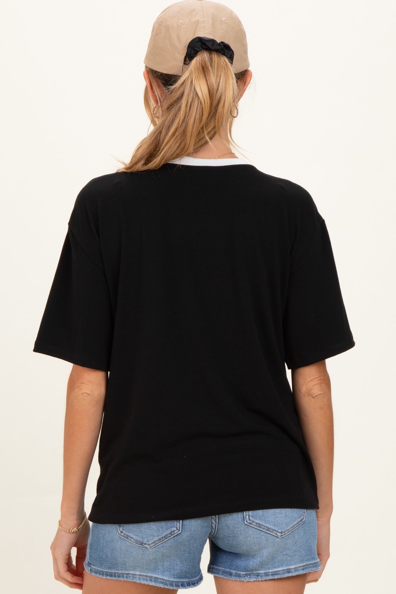 woman wearing a black oversized maternity t-shirt with a white collar and denim shorts, showing her back view