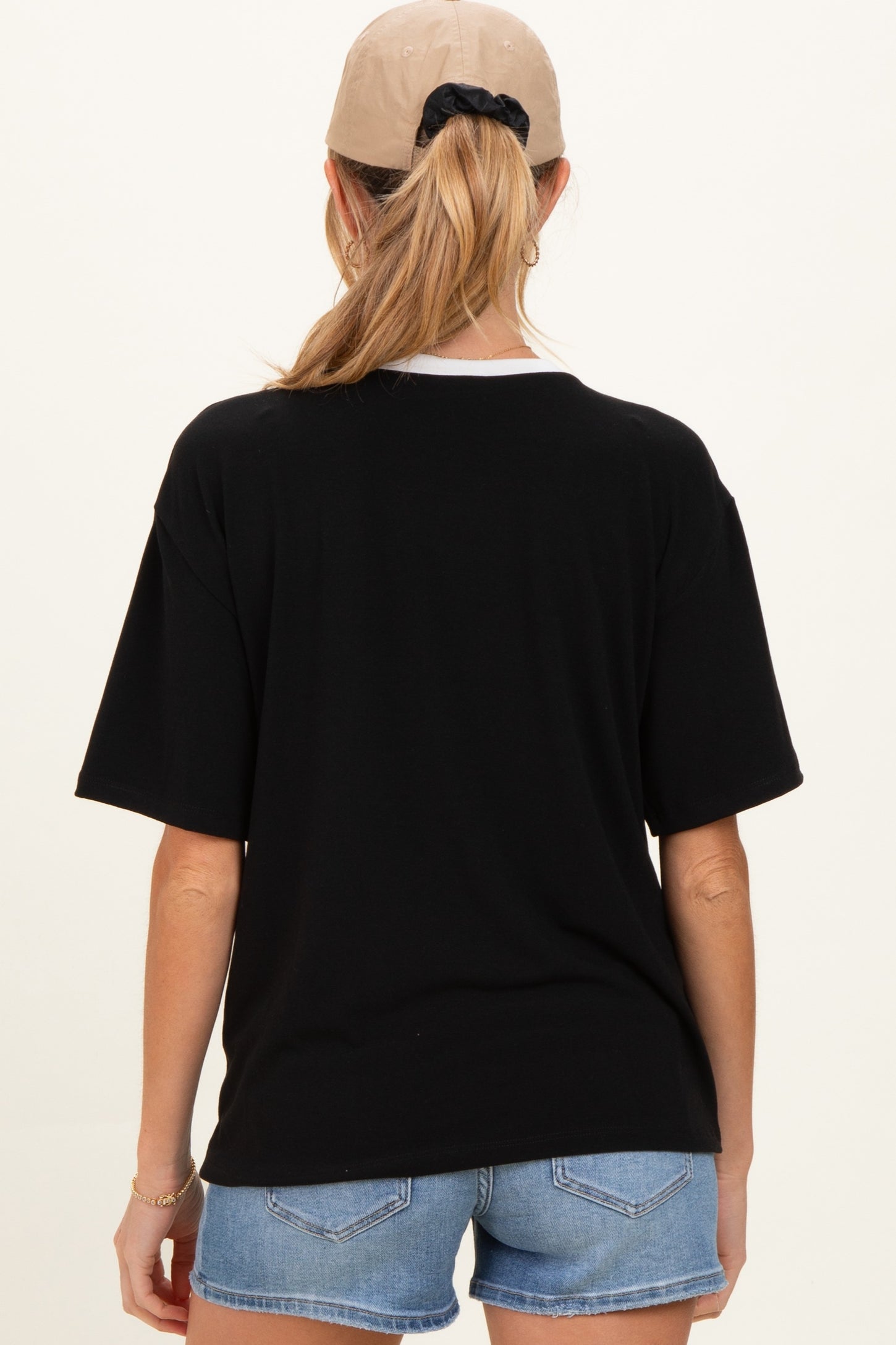 woman wearing a black oversized maternity t-shirt with a white collar and denim shorts, showing her back view