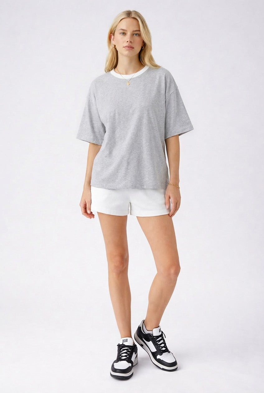 woman wearing a gray short sleeve t-shirt with a white neckline and white shorts, paired with black and white sneakers
