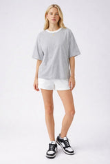 woman wearing a gray short sleeve t-shirt with a white neckline and white shorts, paired with black and white sneakers