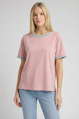 woman wearing a pink short sleeve t-shirt with turquoise trim and side slits, paired with light blue jeans