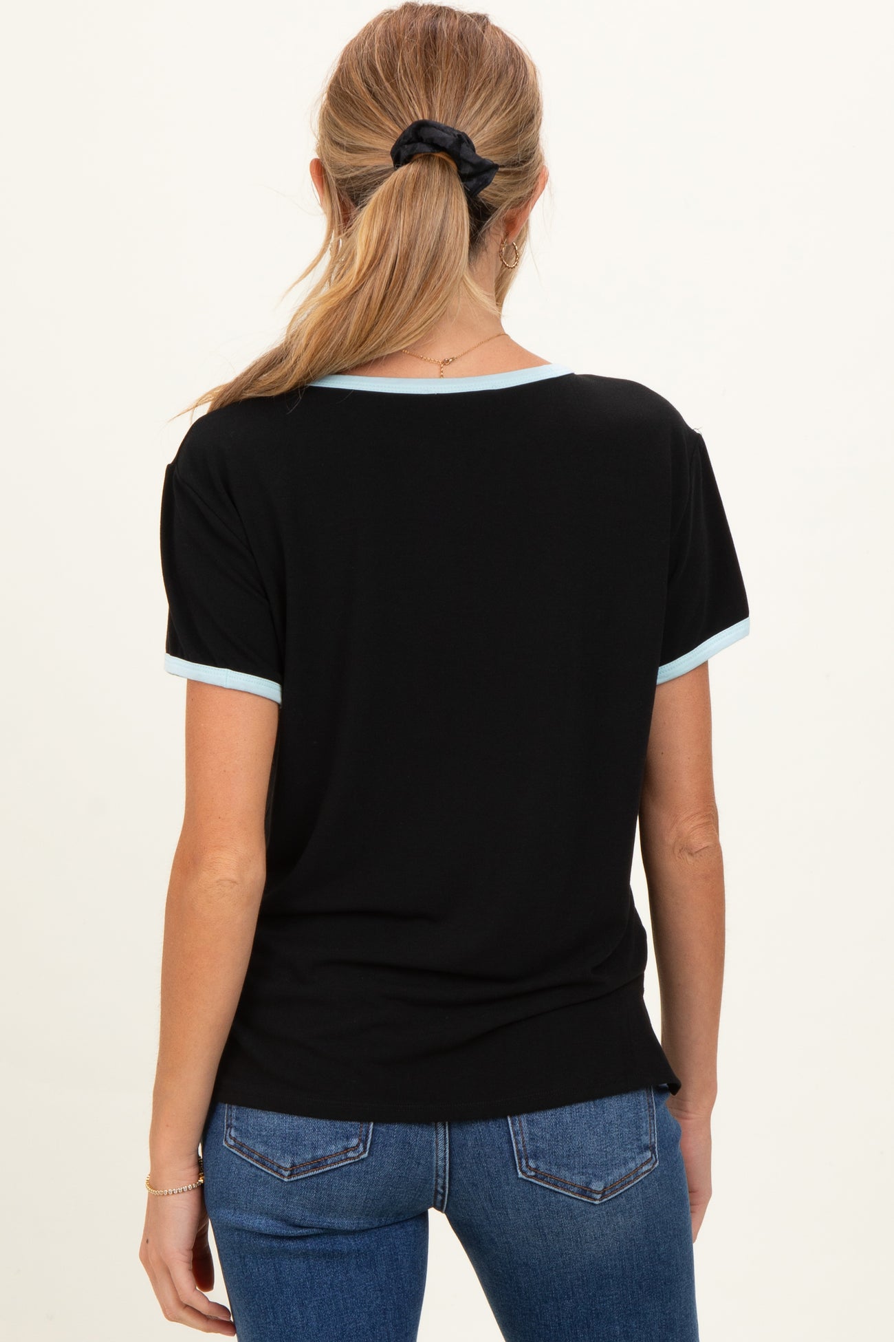 woman wearing a black maternity top with light blue trim, seen from the back, paired with blue jeans