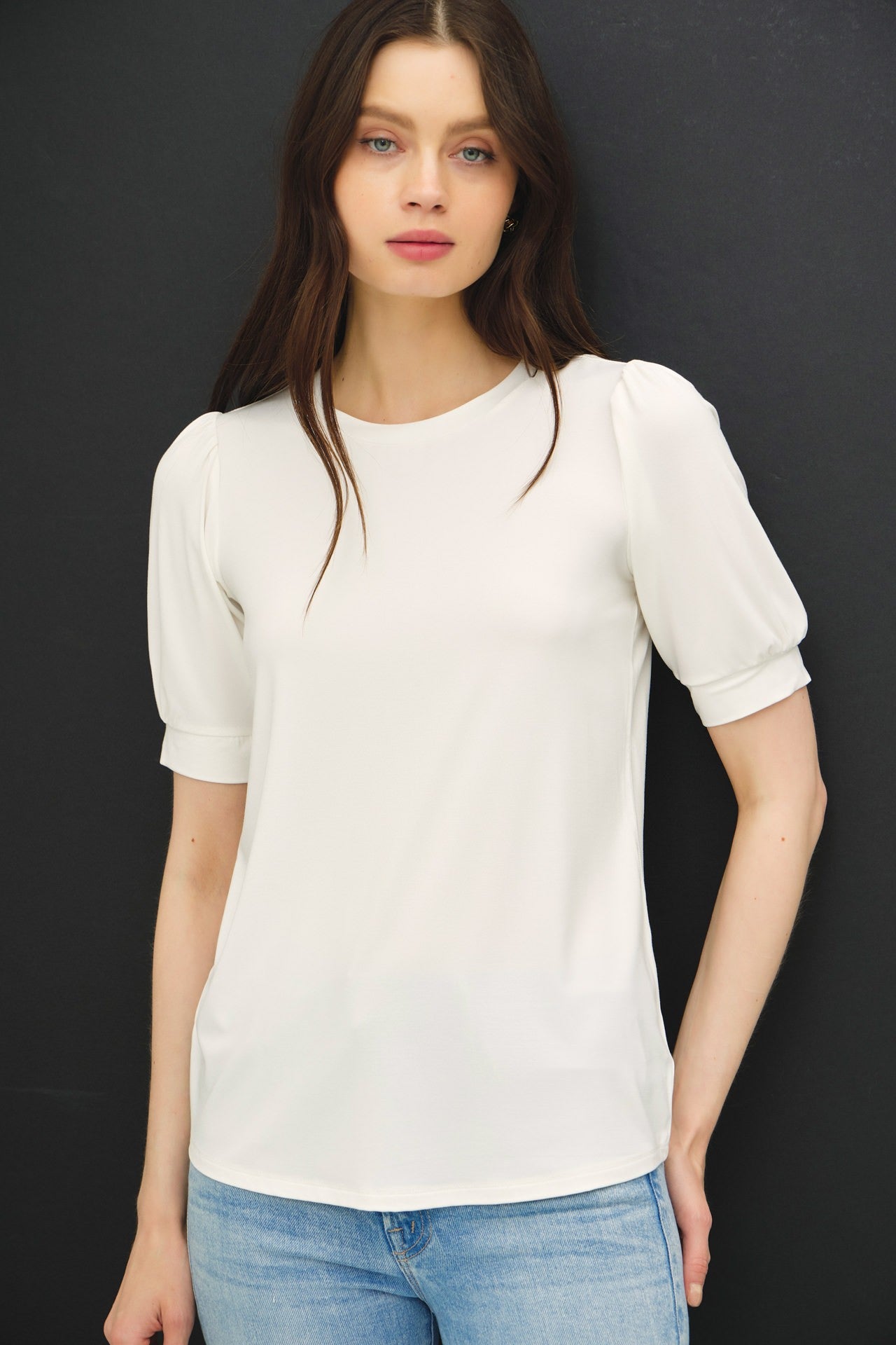 woman wearing a white short sleeve top with puff sleeves and a relaxed fit paired with light blue jeans