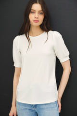 woman wearing a white short sleeve top with puff sleeves and a relaxed fit paired with light blue jeans