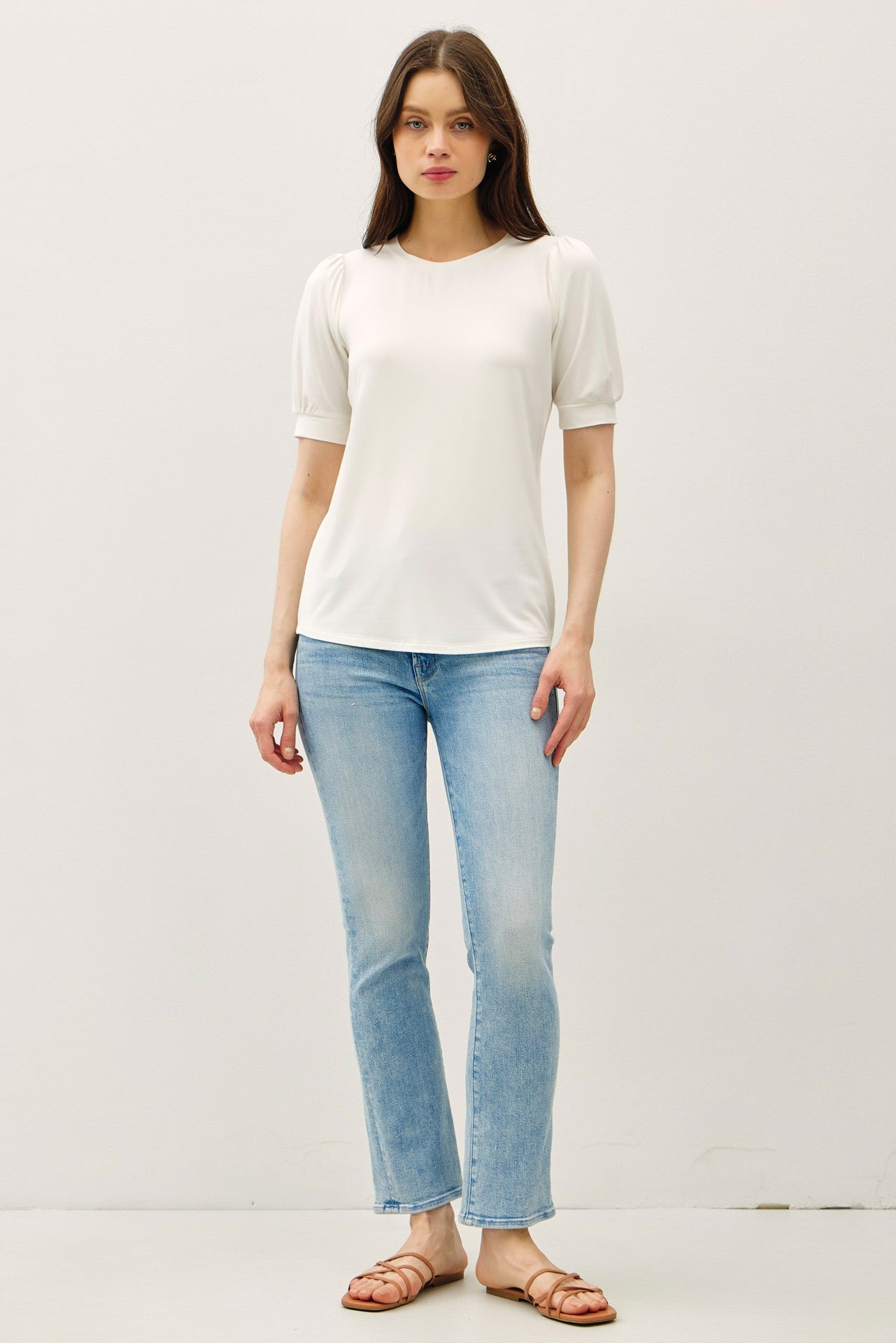 woman wearing a white short sleeve top with puff sleeves and light blue flared jeans