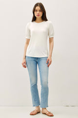 woman wearing a white short sleeve top with puff sleeves and light blue flared jeans