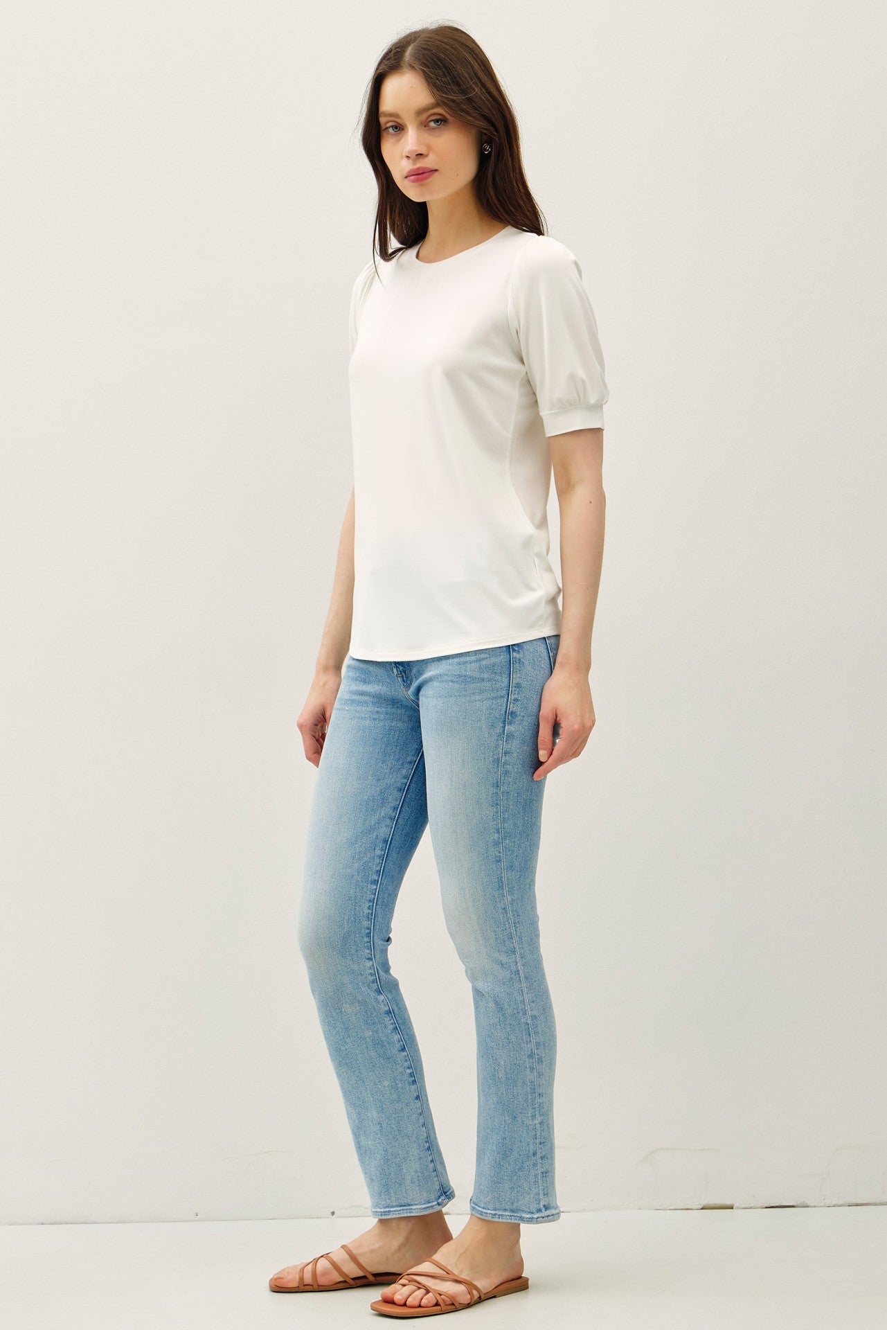 woman wearing a white short sleeve top with puff sleeves and light blue flared jeans, standing in a casual pose