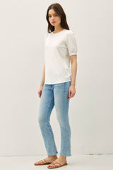 woman wearing a white short sleeve top with puff sleeves and light blue flared jeans, standing in a casual pose