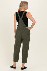 woman wearing an olive green overall jumpsuit with adjustable straps and side pockets, seen from the back