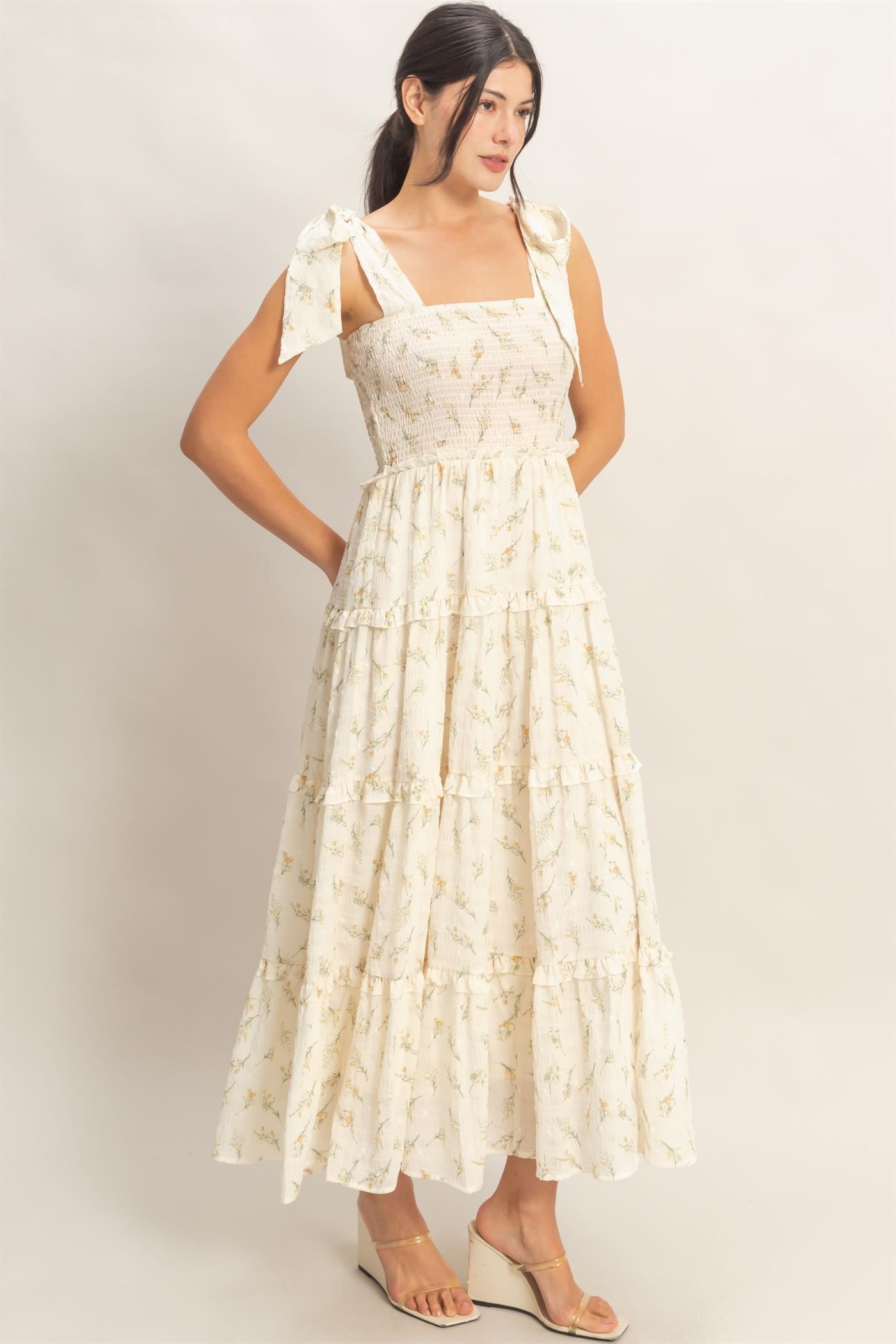 woman wearing a cream floral print maxi dress with bow tie straps and tiered ruffles