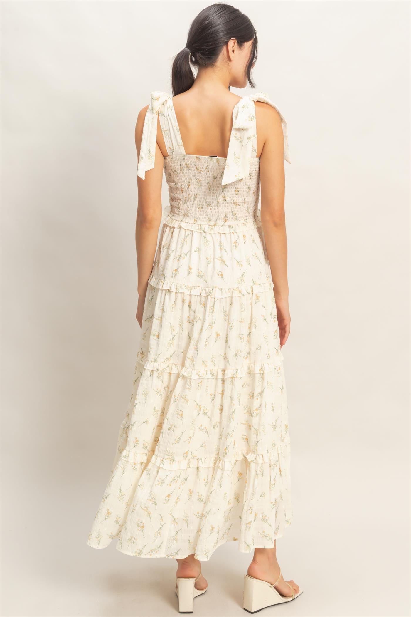 woman wearing a white floral maxi dress with tie shoulder straps and a tiered skirt, shown from the back