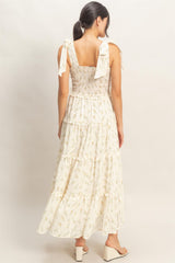 woman wearing a white floral maxi dress with tie shoulder straps and a tiered skirt, shown from the back