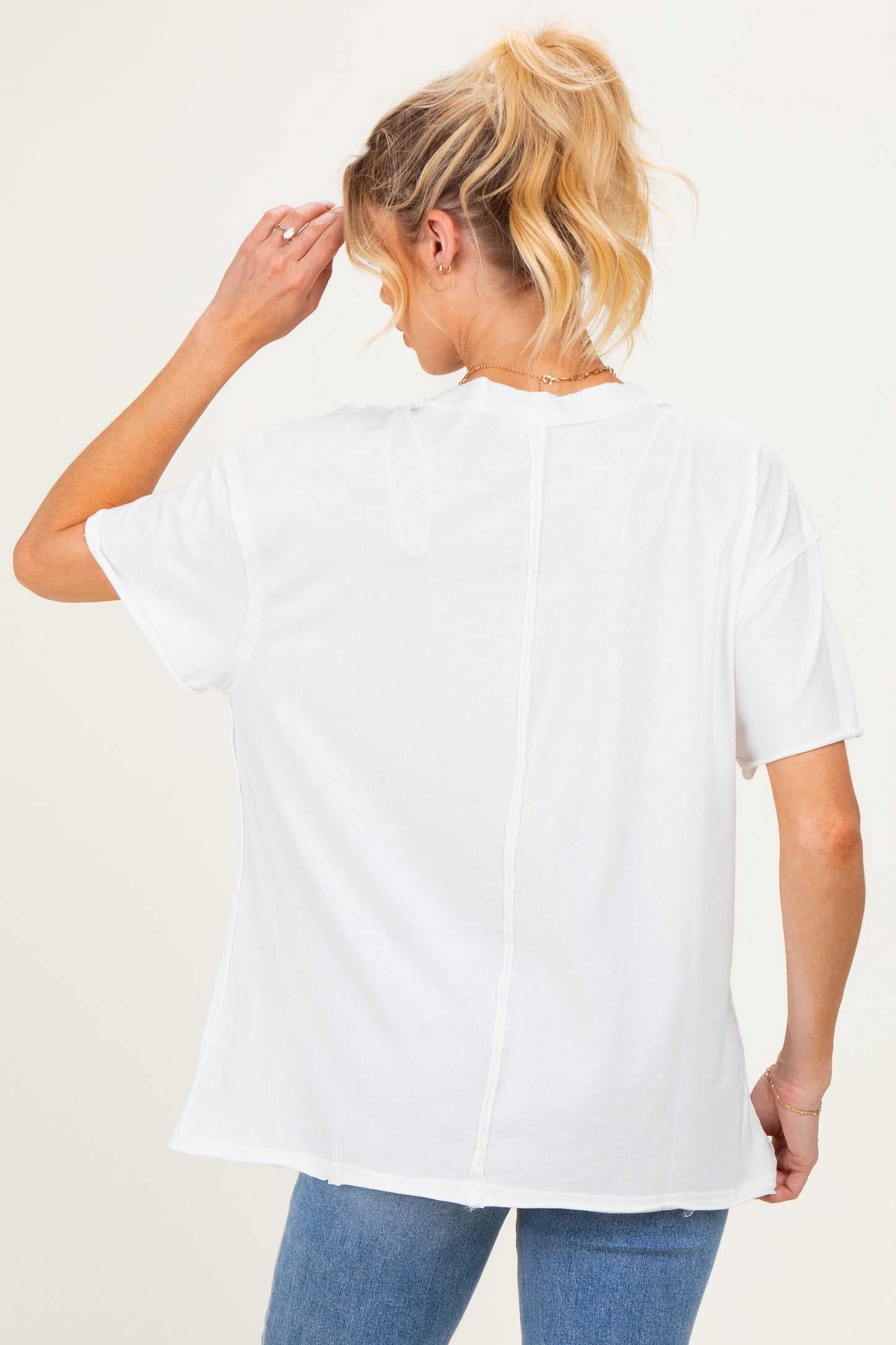 woman wearing a white oversized maternity t-shirt, showing a relaxed fit and back detail, with light blue jeans