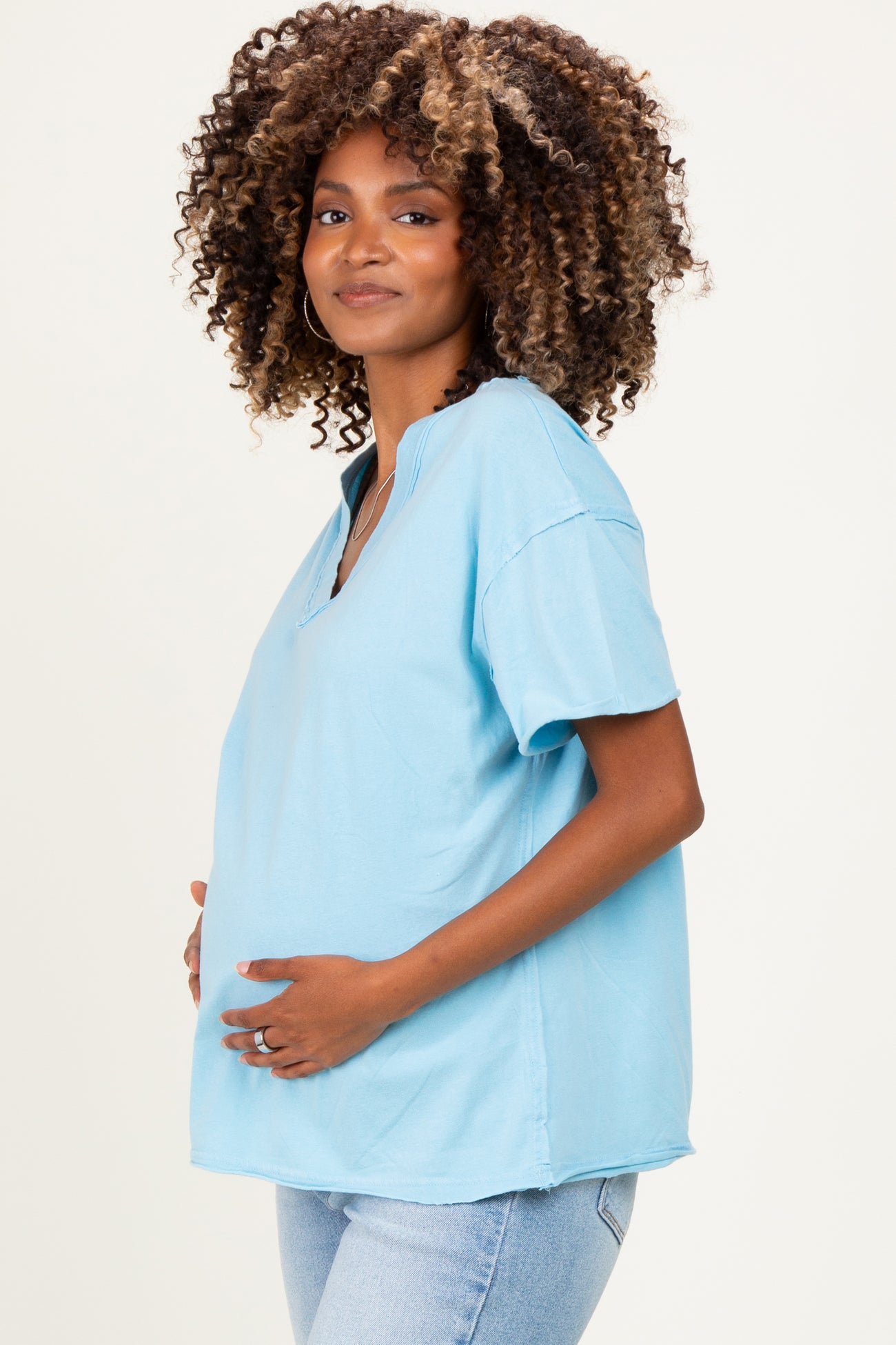 woman wearing a light blue short sleeve maternity top and holding her baby bump